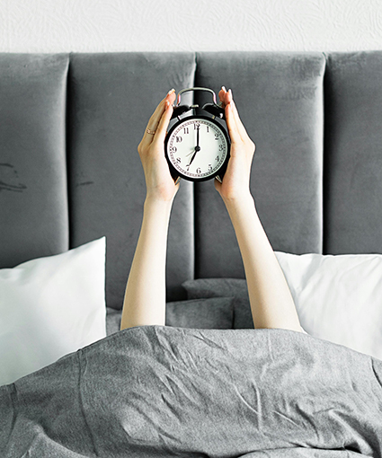 reloj despertador en las manos sobre sábanas grises interviniendo en los ritmos circadianos