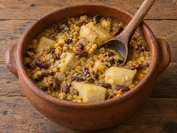 Receta de cachuopa con maíz, ñame y fríjoles en una olla de barro con cuchara de madera